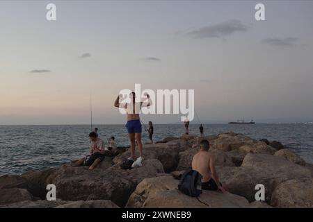 Les gens sont assis sur un brise-lames rocheux à la plage de Bat Galim le 14 août 2024 à Haïfa, Israël. Banque D'Images