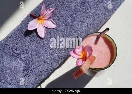 Vue aérienne d'un cocktail rose sur une table avec une serviette enroulée et des fleurs de frangipanier Banque D'Images