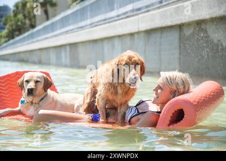 Femme couchée sur un lilo dans l'océan avec deux chiens, Floride, USA Banque D'Images