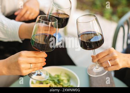 Gros plan de trois femmes serrant des verres de vin rouge tout en se relaxant sur la terrasse d'été Banque D'Images