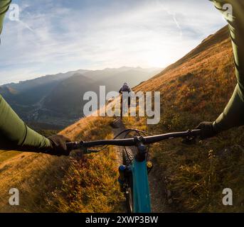 Perspective personnelle d'un homme suivant une femme VTT au coucher du soleil, Gastein Valley, Salzbourg, Autriche Banque D'Images