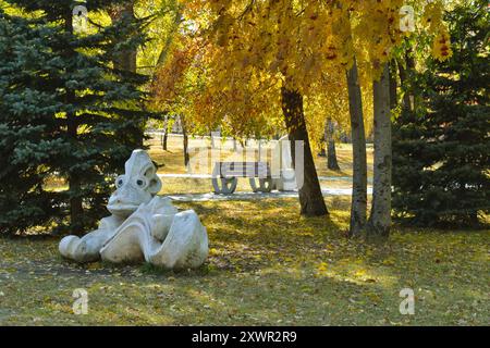 Une sculpture d'une étrange créature et un banc dans un parc d'automne baigné de soleil Banque D'Images