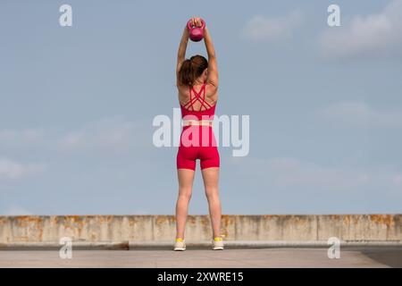 Fit femme sportive exerçant avec un poids kettlebell, à l'extérieur, fond urbain Banque D'Images