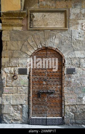 Une porte en bois cloutée sous une plaque commémorative pour la reconstruction du Ponte Vecchio après les inondations de 1333, Florence, Toscane, Italie Banque D'Images