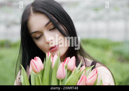 Jeune femme debout dans une grande serre et tenant des tulipes en fleurs dans ses mains. Banque D'Images