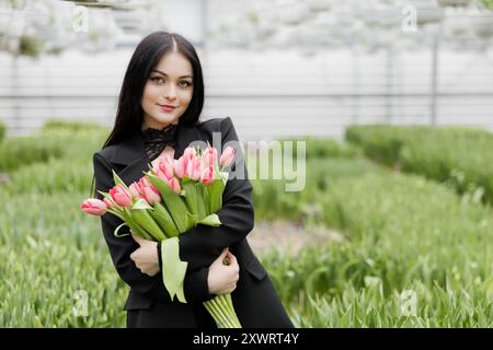 Jeune femme debout dans une grande serre et tenant des tulipes en fleurs dans ses mains. Banque D'Images