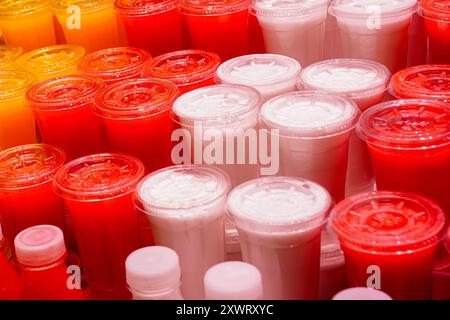 Jus fraîchement pressés de divers fruits dans des gobelets en plastique transparent à un étal de marché, jus frais dans le magasin de fruits Banque D'Images