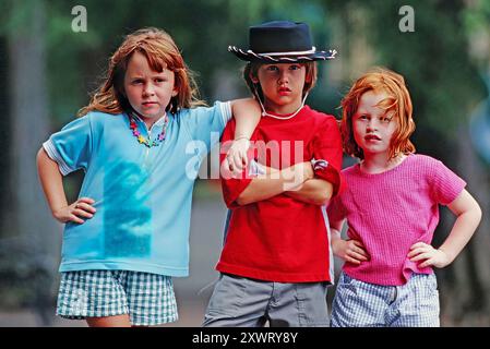 Un portrait de trois enfants debout ensemble avec des expressions fortes, mettant en valeur leur tenue d'été décontractée tout en profitant du plein air. Banque D'Images