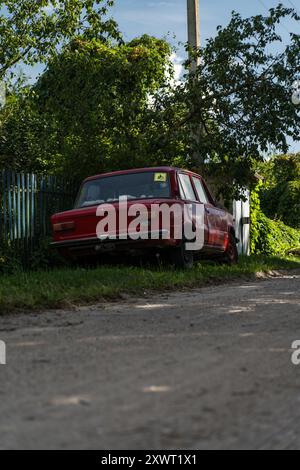 Une voiture rouge soviétique est garée sur le bord de la route dans le village Banque D'Images