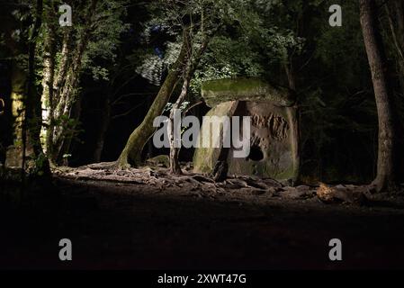 Une scène nocturne mystique capture un ancien dolmen dans la région de Gelendzhik en Russie. Illuminée par un éclairage doux, la structure en pierre se dresse au milieu d'une forêt sereine. Banque D'Images