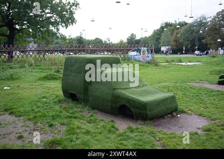 Une sculpture de voiture unique recouverte d'herbe dans un parc berlinois agit comme une métaphore de la nature qui récupère des espaces urbains. Cette image évoque les thèmes de la durabilité, de la sensibilisation à l'environnement et de l'intersection de la nature et de l'innovation humaine. Banque D'Images