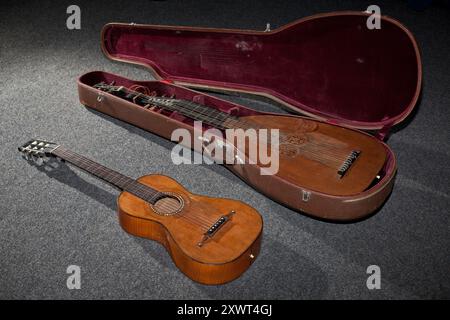 Une guitare antique se trouve à côté d'un luth dans un étui ouvert sur un tapis gris. L’image évoque un sentiment d’héritage musical, de tradition et de passage du temps. Banque D'Images