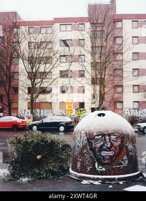 Un arbre de Noël abandonné se trouve à côté d'un bac de recyclage couvert de graffitis un jour d'hiver dans un quartier urbain, symbolisant la négligence après les vacances et la décomposition urbaine. Banque D'Images