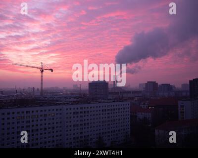 Une belle aube à Berlin avec un ciel rose, smokestack industriel et grue de construction. La scène reflète un mélange de développement urbain et d'impact environnemental, symbolisant le progrès et les défis. Banque D'Images