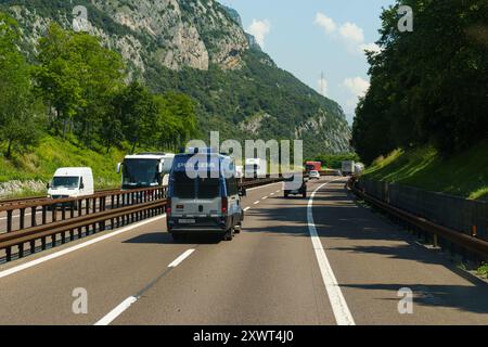 Ossenigo, Italie - 8 juin 2023 : un véhicule de police circule sur une autoroute, flanqué de camions et de bus sous un ciel bleu clair, avec des montagnes servant de Banque D'Images