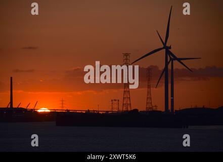 Un coucher de soleil sur la Tamise près de Gravesend dans le Kent silhouette les quais et les grues du port de Tilbury. Banque D'Images