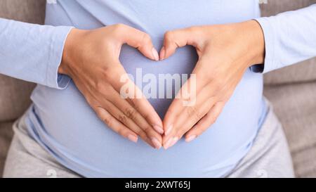 Femme enceinte méconnaissable tenant les mains sur le ventre formant le cœur, vue de dessus Banque D'Images