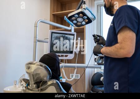 Conversation entre un dentiste et une femme musulmane portant le hijab regardant ses dents radiographie à l'écran et le médecin décrit son traitement Banque D'Images