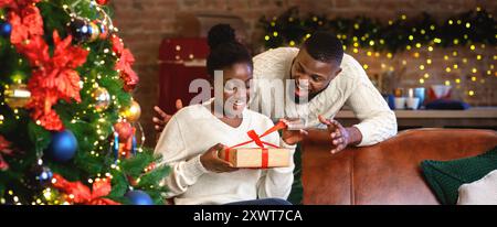 Femme noir excité déballer cadeau de Noël de son mari Banque D'Images