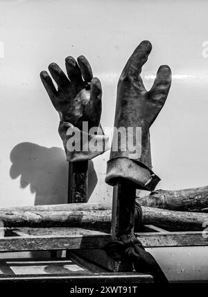 Paire de gants de travailleur en caoutchouc sale : environnement de service public isolé sur fond blanc - lumière et ombre. Noir et blanc. Banque D'Images