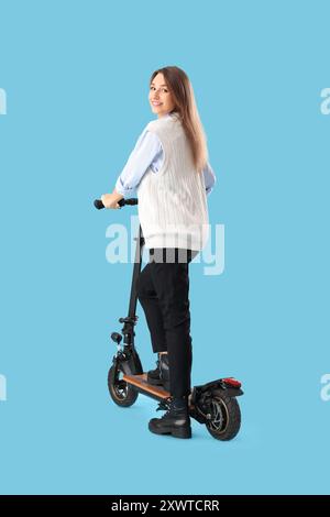 Jeune femme d'affaires chevauchant scooter électrique sur fond bleu Banque D'Images