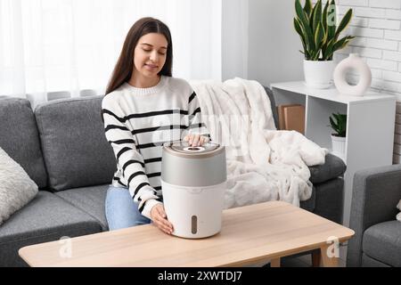 Jeune femme assise sur un canapé noir et allumant l'humidificateur moderne dans le salon Banque D'Images