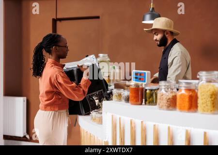 Fournisseur emballant des produits bio biologiques dans un sac thermique pour la livraison à domicile de produits d'épicerie. Un employé afro-américain arrive pour ramasser des fruits et légumes pour les clients des magasins écologiques locaux. Banque D'Images