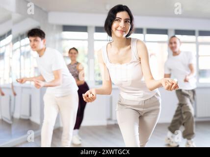 Fille aime la danse active, apprend de nouveaux mouvements, se déplace de manière synchrone avec les participants de la leçon Banque D'Images