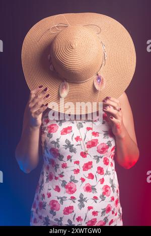 Belle femme debout portant une robe colorée avec un chapeau couvrant toute sa tête. Isolé sur fond fumé coloré. Banque D'Images