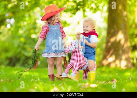 Petit garçon et fille habillés comme cow-boy et cow-girl jouant avec jouet cheval à bascule dans le parc. Les enfants jouent à l'extérieur. Enfants en costumes d'Halloween Banque D'Images