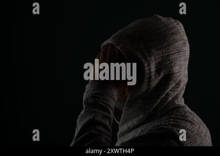 Gros plan portrait d'un homme mystérieux portant des lunettes de soleil et un sweat-shirt à capuche couvrant la tête avec les mains sur le visage. Isolé sur fond sombre. Banque D'Images