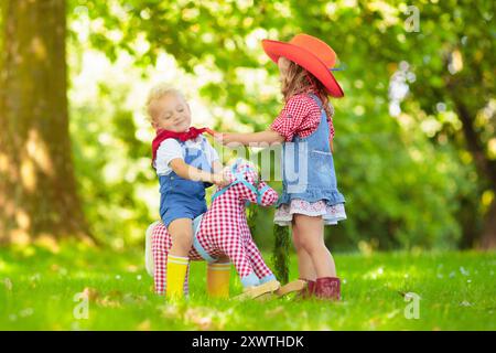 Petit garçon et fille habillés comme cow-boy et cow-girl jouant avec jouet cheval à bascule dans le parc. Les enfants jouent à l'extérieur. Enfants en costumes d'Halloween Banque D'Images