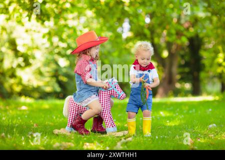 Petit garçon et fille habillés comme cow-boy et cow-girl jouant avec jouet cheval à bascule dans le parc. Les enfants jouent à l'extérieur. Enfants en costumes d'Halloween Banque D'Images