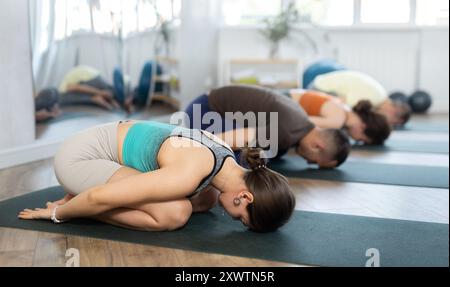 Les amateurs de mode de vie actif sur tapis de yoga effectuent la version faisant de la pose d'enfant dans le gymnase Banque D'Images