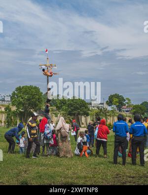 Balikpapan, Indonésie - 18 août 2024. Le grimpeur masculin est encouragé par la foule pendant la compétition d'escalade de palmiers ou de panjat pinang. Banque D'Images