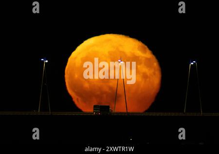 La pleine lune se lève de la structure du pont Vasco da Gama à Lisbonne. La Lune bleue, nommée d'après la deuxième pleine lune au cours du même mois du calendrier grégorien, est la première de 2024 et a la particularité d'orbiter près de 22 mille kilomètres plus près de la Terre. Banque D'Images