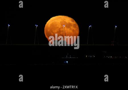 La pleine lune se lève de la structure du pont Vasco da Gama à Lisbonne. La Lune bleue, nommée d'après la deuxième pleine lune au cours du même mois du calendrier grégorien, est la première de 2024 et a la particularité d'orbiter près de 22 mille kilomètres plus près de la Terre. Banque D'Images