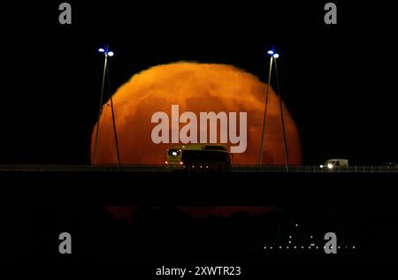 La pleine lune se lève de la structure du pont Vasco da Gama à Lisbonne. La Lune bleue, nommée d'après la deuxième pleine lune au cours du même mois du calendrier grégorien, est la première de 2024 et a la particularité d'orbiter près de 22 mille kilomètres plus près de la Terre. Banque D'Images