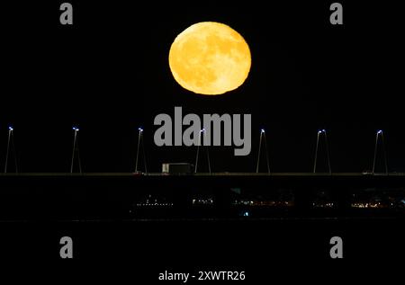 La pleine lune se lève de la structure du pont Vasco da Gama à Lisbonne. La Lune bleue, nommée d'après la deuxième pleine lune au cours du même mois du calendrier grégorien, est la première de 2024 et a la particularité d'orbiter près de 22 mille kilomètres plus près de la Terre. Banque D'Images