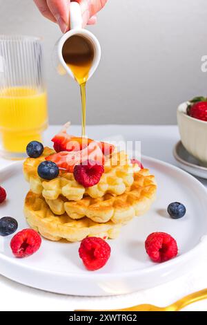Délicieuses gaufres maison garnies de baies fraîches et de sirop d'érable sur une table de petit déjeuner Banque D'Images