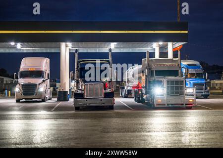 Semi-remorques de grande taille de qualité industrielle avec différentes semi-remorques chargées garées pour le conducteur de camion se reposer sous un abri couvert éclairé sur l'arrêt de camion p Banque D'Images