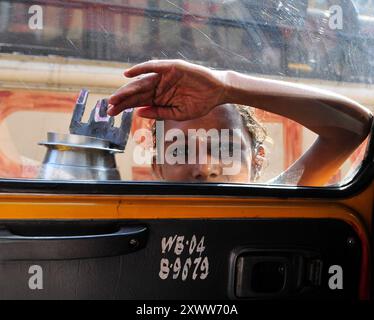 Un jeune mendiant frappant à la fenêtre et des taxis dans une rue animée de Kolkata, en Inde. Banque D'Images