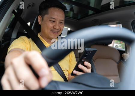 Homme joyeux conducteur arabe texturant sur smartphone tout en conduisant la voiture. transport, véhicule et concept de technologie - homme souriant ou conducteur conduisant la voiture et nous Banque D'Images