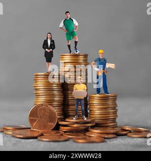 Personnes de diverses professions sur des piles de pièces de différentes hauteurs sur fond gris Banque D'Images