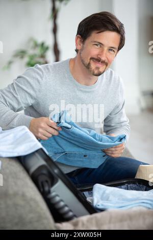 homme heureux sur le canapé préparant le retour de voyage et la valise d'emballage Banque D'Images