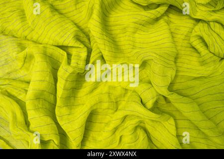 Un tissu en lin vert citron éclatant aux rayures subtiles est drapé de plis doux et naturels. Le gros plan met en valeur la texture et la riche couleur du fabr Banque D'Images