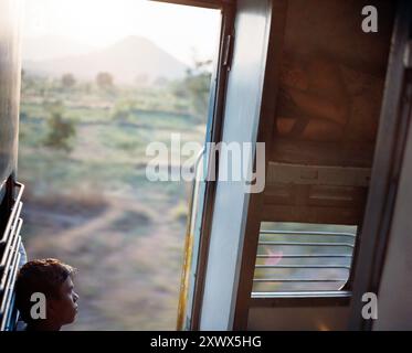 Un garçon contemplatif regardant par une fenêtre de train pendant un voyage de Goa à Mumbai en Inde. Capture un moment de réflexion et la nature transitoire du voyage de la vie. Banque D'Images