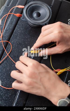 Gros plan des mains travaillant sur un câblage électrique se connectant à un haut-parleur sur une surface noire. Cette image représente métaphoriquement le lien entre l'innovation et l'application pratique dans l'électronique et l'ingénierie. Banque D'Images