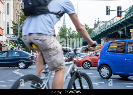 Une scène de pointe matinale trépidante à l'U-Bahnhof Eberswalderstr. À Berlin-Prenzlauer Berg avec un cycliste naviguant dans la circulation dense avec des voitures qui l'entourent. L'image capture la nature chaotique des déplacements urbains dans un environnement urbain animé. Banque D'Images