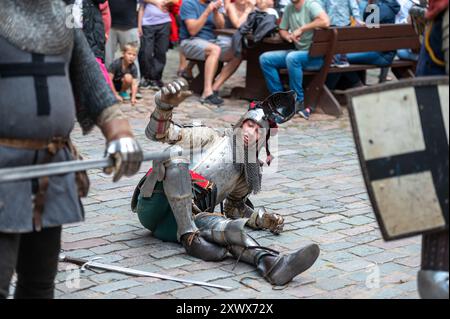 Jaunpils, Lettonie - 10 août 2024 : un chevalier tombe au sol alors que les spectateurs acclament à proximité. Banque D'Images